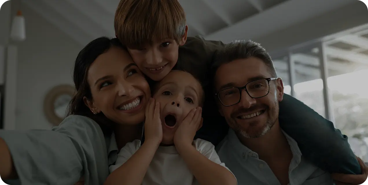 A happy family lying together on a bed, smiling while taking a selfie with a smartphone.