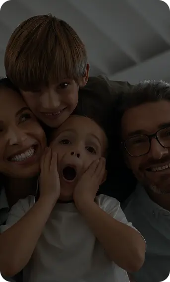 A happy family lying together on a bed, smiling while taking a selfie with a smartphone.